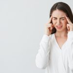 Young beautiful brunette businesswoman holding fingers on temples frowning from pain over white background. Headache. Copy space.